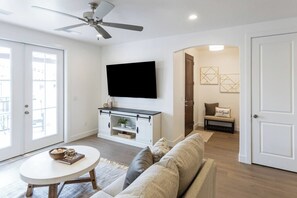 A living room with a flat-screen TV, a sofa, a coffee table, and a ceiling fan.