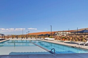 A swimming pool with lounge chairs, a covered seating area, and a view of a mountainous landscape.