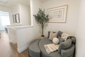 A modern living room with a grey sofa, a potted plant, and framed artwork on the wall.