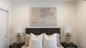Een slaapkamer met een bed, twee nachtkastjes met lampen, een abstract schilderij aan de muur en een deur.