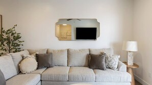 Een woonkamer met een bank, een aan de muur bevestigde televisie en een lamp.