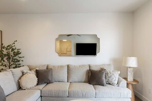 Ein Wohnzimmer mit einer Couch, einem Wandfernseher und einer Lampe.