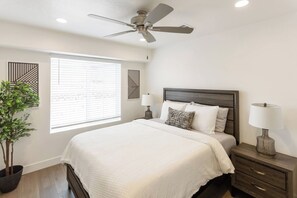 A bedroom with a bed, bedside lamps, a ceiling fan, a window with blinds, and a potted plant. - Heated Pool & Pickleball near National and State Parks (Washington)