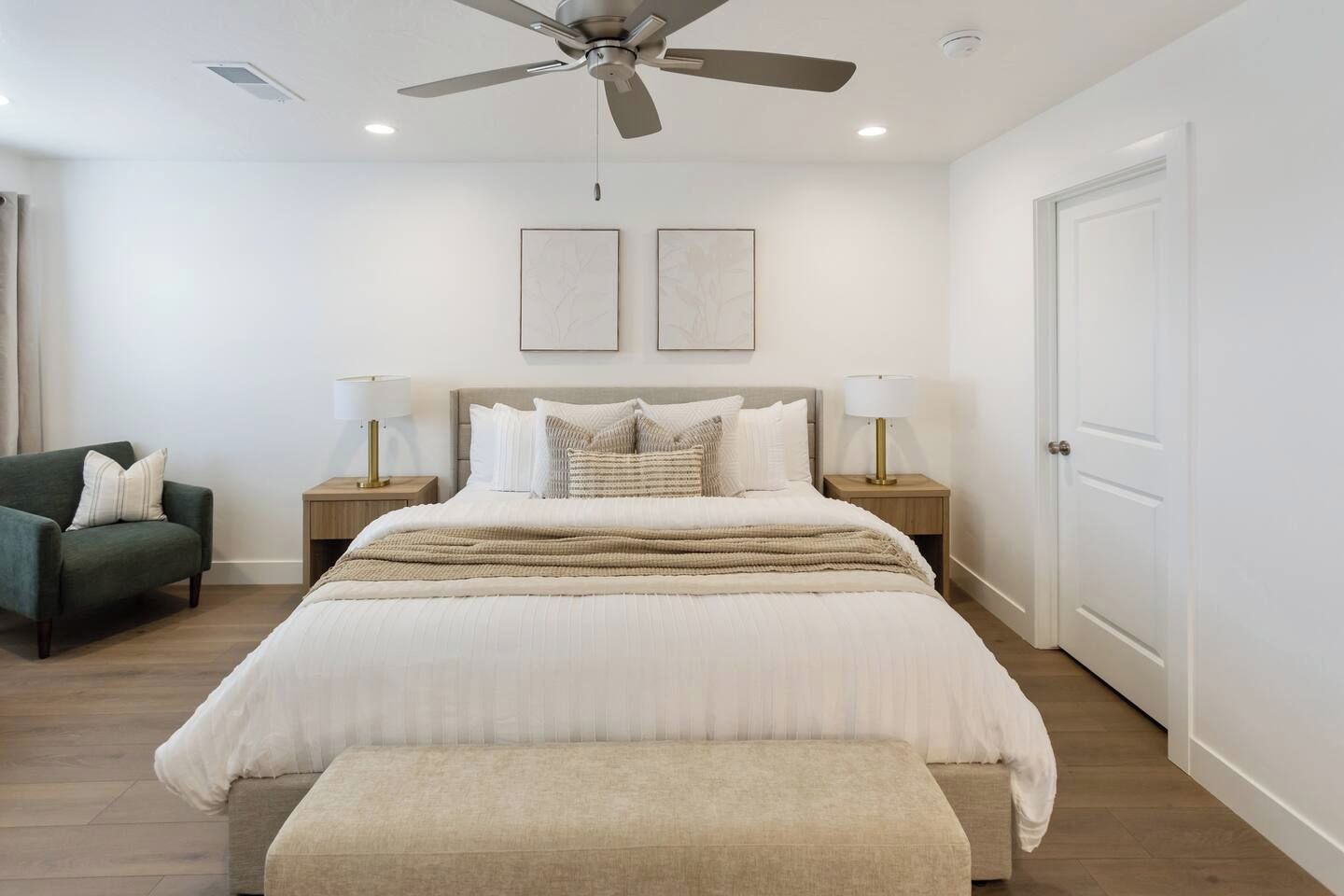 A bedroom with a bed, two bedside lamps, a ceiling fan, and a door.