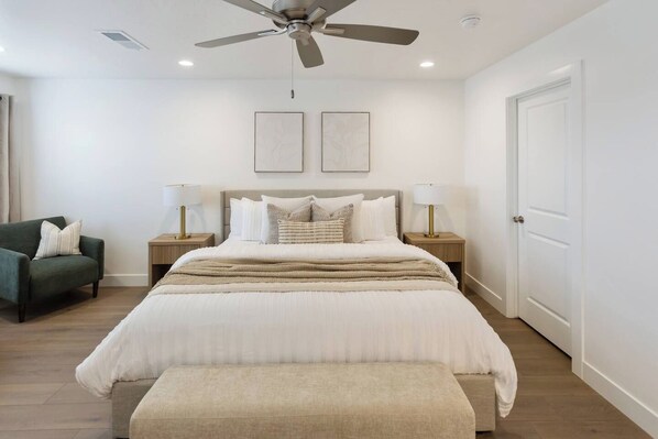A bedroom with a bed, two bedside lamps, a ceiling fan, and a door.