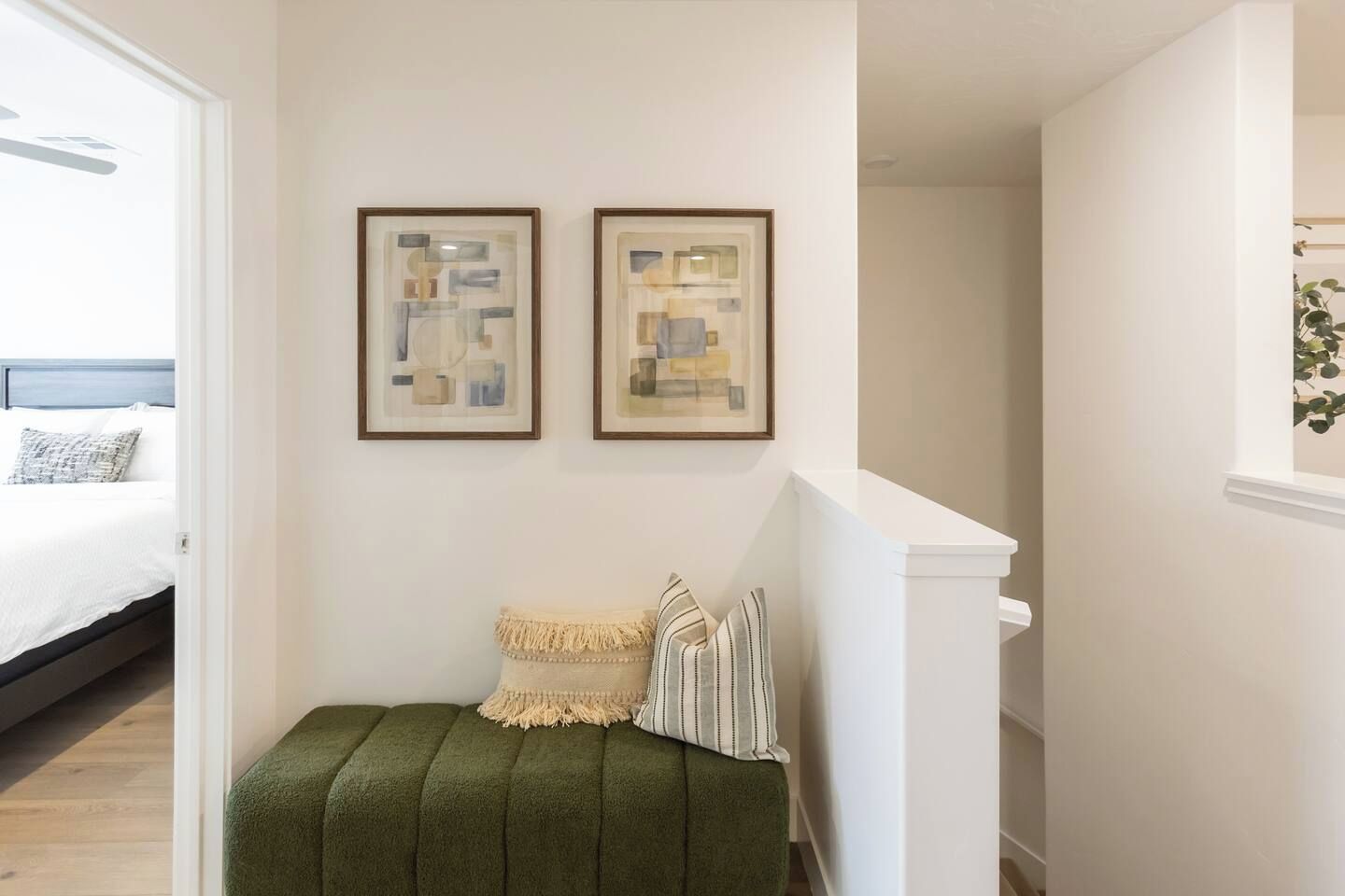 Un dormitorio con cama, un banco tapizado de verde, dos cuadros abstractos enmarcados y una escalera.