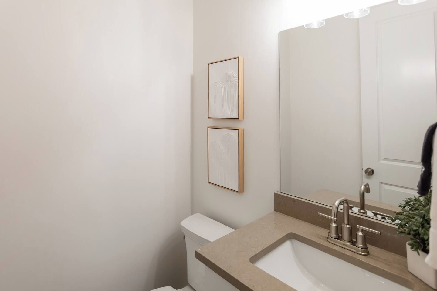 A bathroom with a toilet, sink, and mirror. There are two framed pictures on the wall.