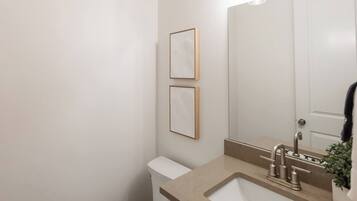 A bathroom with a toilet, sink, and mirror. There are two framed pictures on the wall.