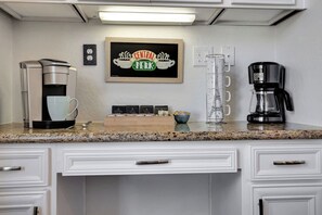 Eine Küche mit Kaffeemaschine, Kaffeekanne, einem gerahmten Schild und einer Ablage mit Kaffeekapseln.