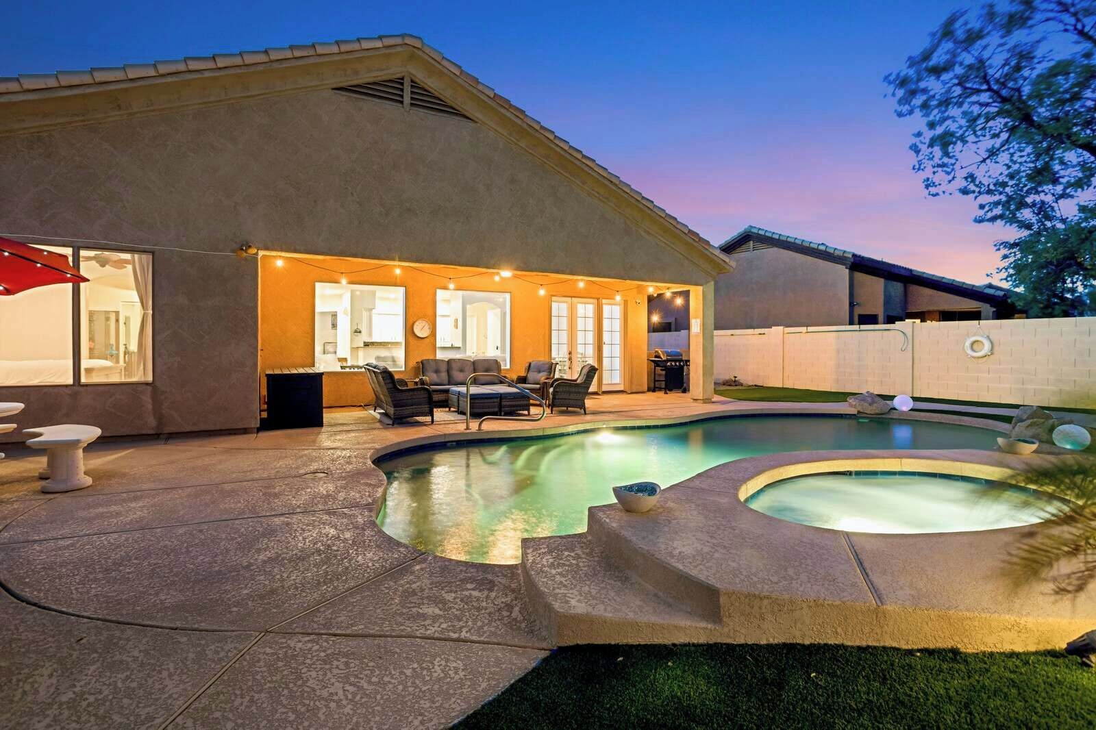 Un patio trasero con piscina, mobiliario de exterior y un área de terraza cubierta.
