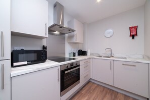 A modern kitchen with white cabinets, a stainless steel range hood, a microwave, a coffee maker, and a clock on the wall. - 1BR Hull Old Town Apartment | Near Museums Quarter (Kingston upon Hull)