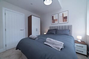 Ein Schlafzimmer mit einem Bett, einem Kleiderschrank, einem Nachttisch und zwei an der Wand befestigten Bilderrahmen.