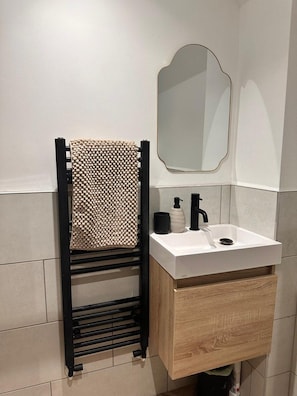 Un bany amb penjador de tovalloles, un lavabo, un mirall i un armari de fusta.