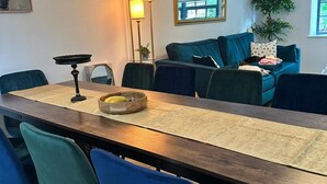 Ein Essbereich mit einem langen Tisch, blauen Stühlen und einer Couch im Hintergrund.
