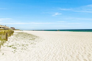 Ein sandiger Strand mit einer Holzlattenzaun und Gebäuden im Hintergrund.