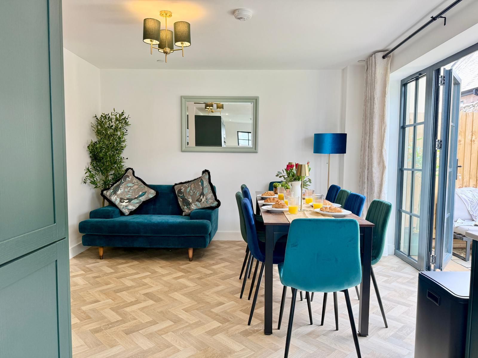 Un coin repas avec une table dressée pour deux personnes, un canapé avec des coussins et une grande fenêtre avec des rideaux.