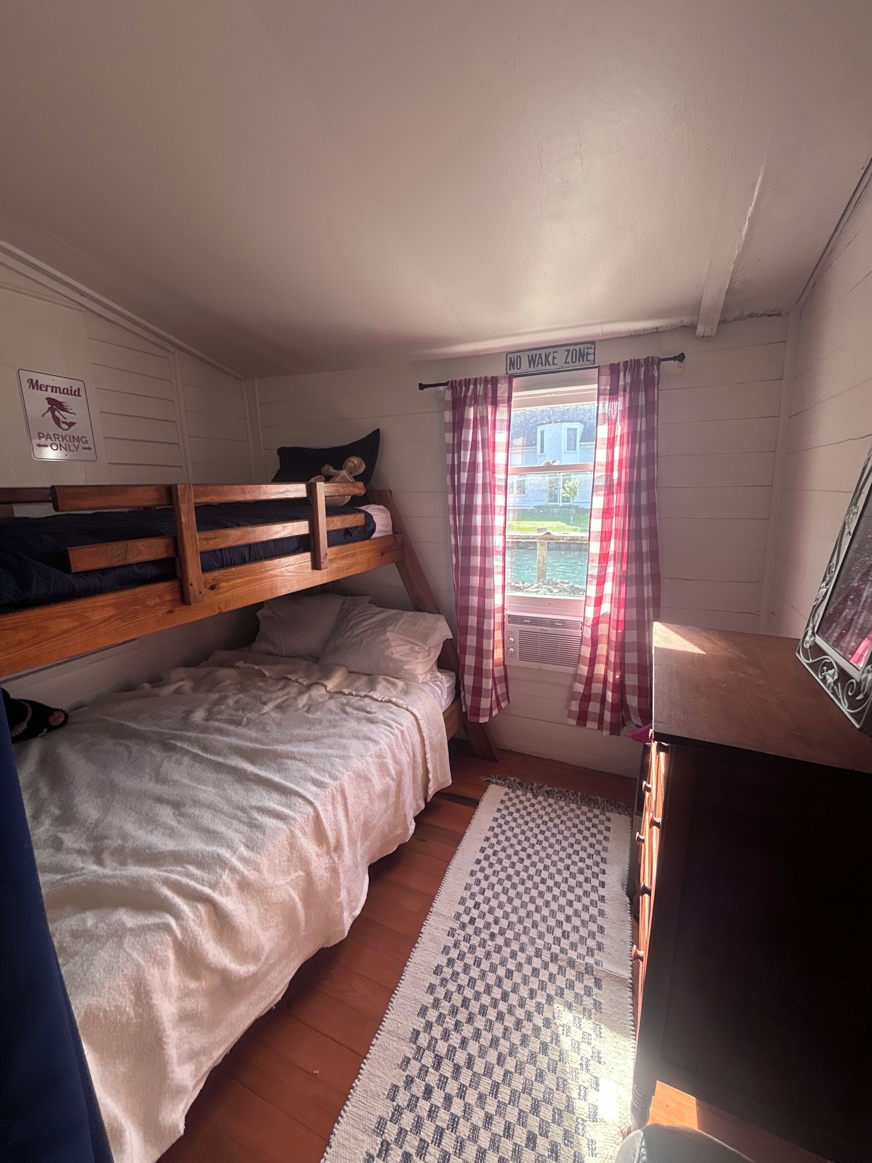 Une chambre avec un lit superposé, une fenêtre avec des rideaux, un radiateur et un panneau indiquant un espace de stationnement.