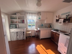 A compact kitchen with a window, a sink, a stove, and a chair.