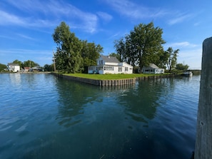 Una casa sobre un muelle con una zona verde y un barco al fondo.