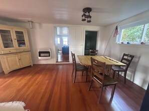 Un comedor con una mesa y sillas de madera, una ventana con una bandera estadounidense y vistas al exterior.