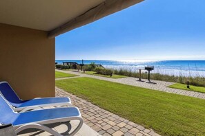 A covered outdoor area with a view of the sea, a paved pathway, and a seating area with chairs. - Coral Reef Ground level unit 10 Epic Views! (Destin)