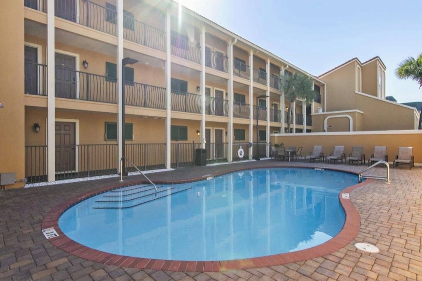 A hotel with a swimming pool, multiple balconies, and a brick-paved area.