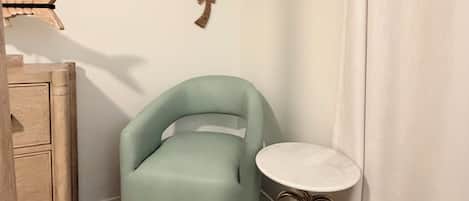A room with a light blue chair, a small round table with a white top, and two wall-mounted decorative items.