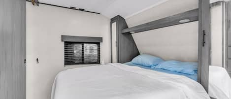 Une chambre avec un lit superposé, une fenêtre avec des stores et un plafond en bois.