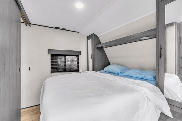 A bedroom with a bunk bed, a window with blinds, and a wooden ceiling.