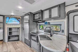 Een kleine camperkeuken met een ingebouwde oven, een magnetron en een spoelbak.