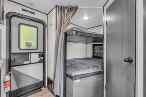 Een compact RV-interieur met een stapelbed, een kleine keukenhoek en een raam met uitzicht.