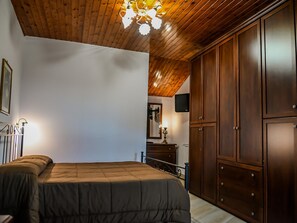 A bedroom with a bed, wooden ceiling, wardrobe, and a small table with a lamp. - Family Sicilian Heritage Home (Trecastagni)