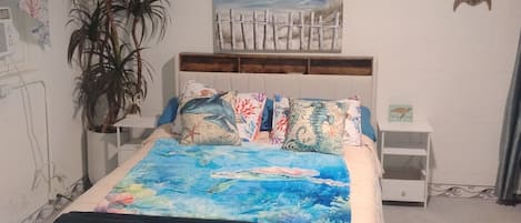Une chambre à coucher comprenant un lit, une table de chevet, une œuvre d’art accrochée au mur, une plante en pot et une petite table.