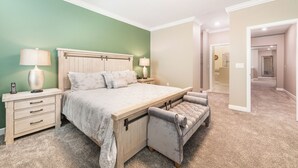 A bedroom with a bed, bedside tables, a lamp, a bench, and a door leading to another room. - Orlando Family Paradise with Private Pool & Resort (Four Corners)