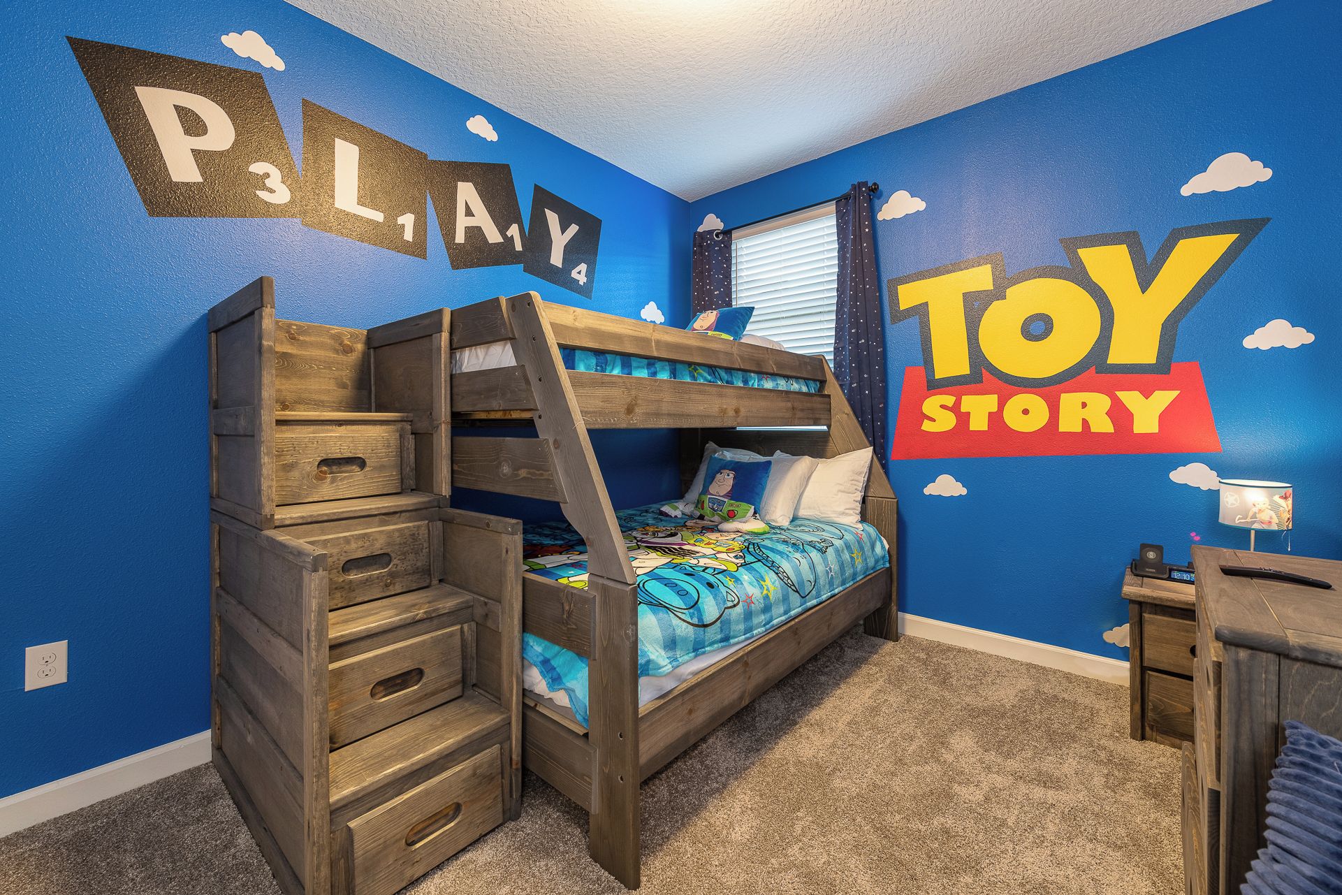 Un lit superposé avec des tiroirs, un bureau et un mur décoré avec des motifs de « Toy Story » et de « P3LAY ».