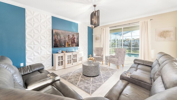 A living room with a blue accent wall, a large TV, leather sofas, a patterned armchair, and a view of a swimming pool. - Orlando Family Paradise with Private Pool & Resort (Four Corners)
