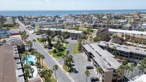A hotel with a parking lot, multiple floors, and a view of the ocean. - 2BR Half Block to Beach, Garage, Heated Pool (South Padre Island)