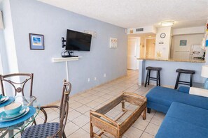 A living room with a TV, a dining area with a glass table, and a kitchen area with stools. - Gulfview - 250 yrds to Beach Bbq Poolside (South Padre Island)