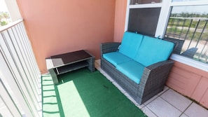 A small outdoor seating area with a wicker sofa and a table, adjacent to a window with a view of greenery. - Gulfview - 250 yrds to Beach Bbq Poolside (South Padre Island)