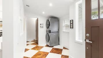 Un corridoio con pavimento a scacchi, una porta con una finestra e un apparecchio fissato al muro.