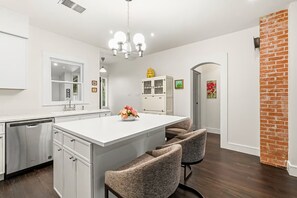 A modern kitchen with white cabinetry, a central island with seating, and a brick accent wall.