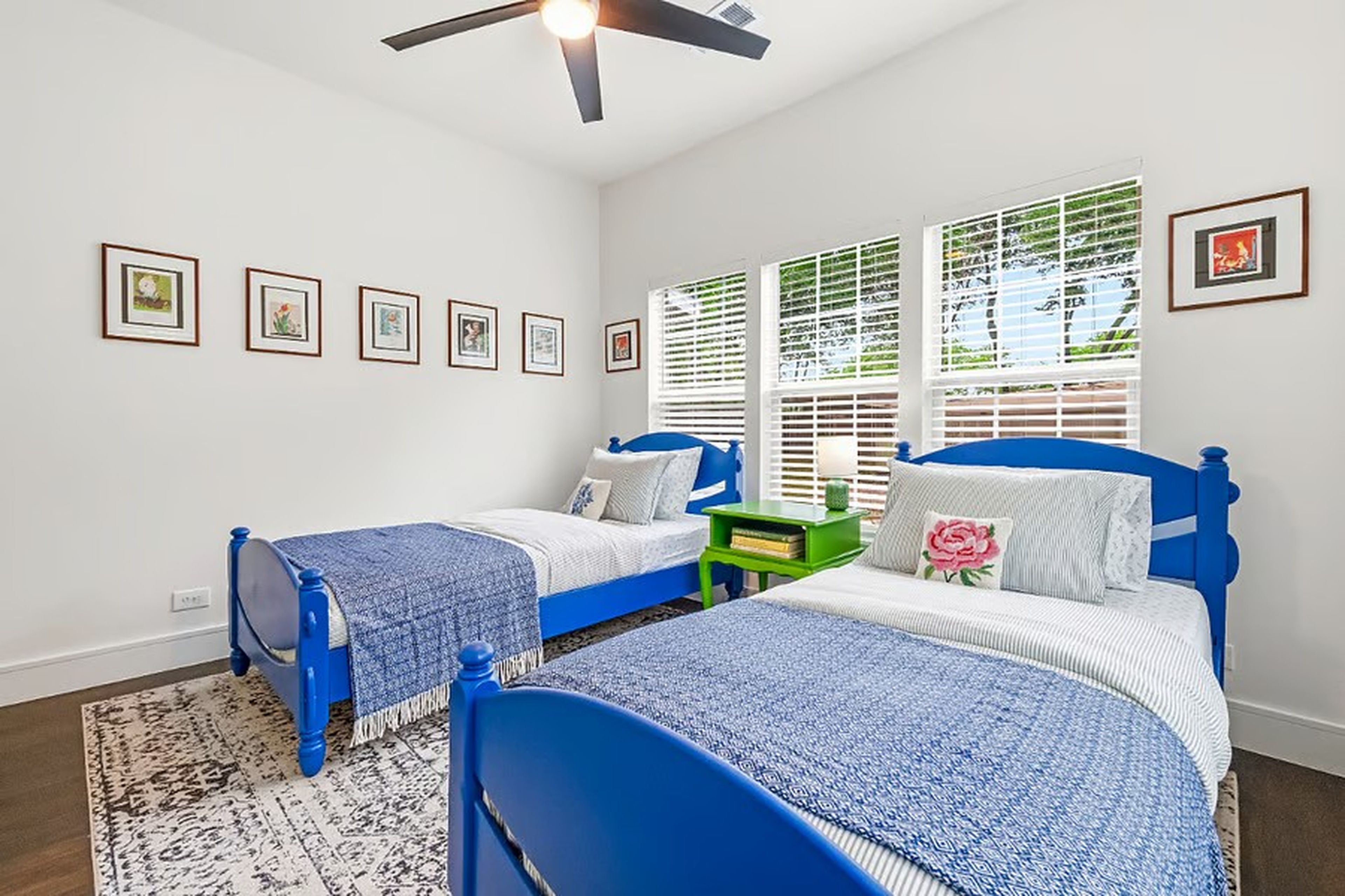 A bedroom with two beds, a ceiling fan, and a window with blinds.