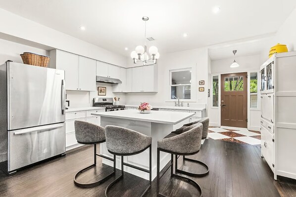 A modern kitchen with white cabinetry, a central island with bar stools, a refrigerator, and a stove.