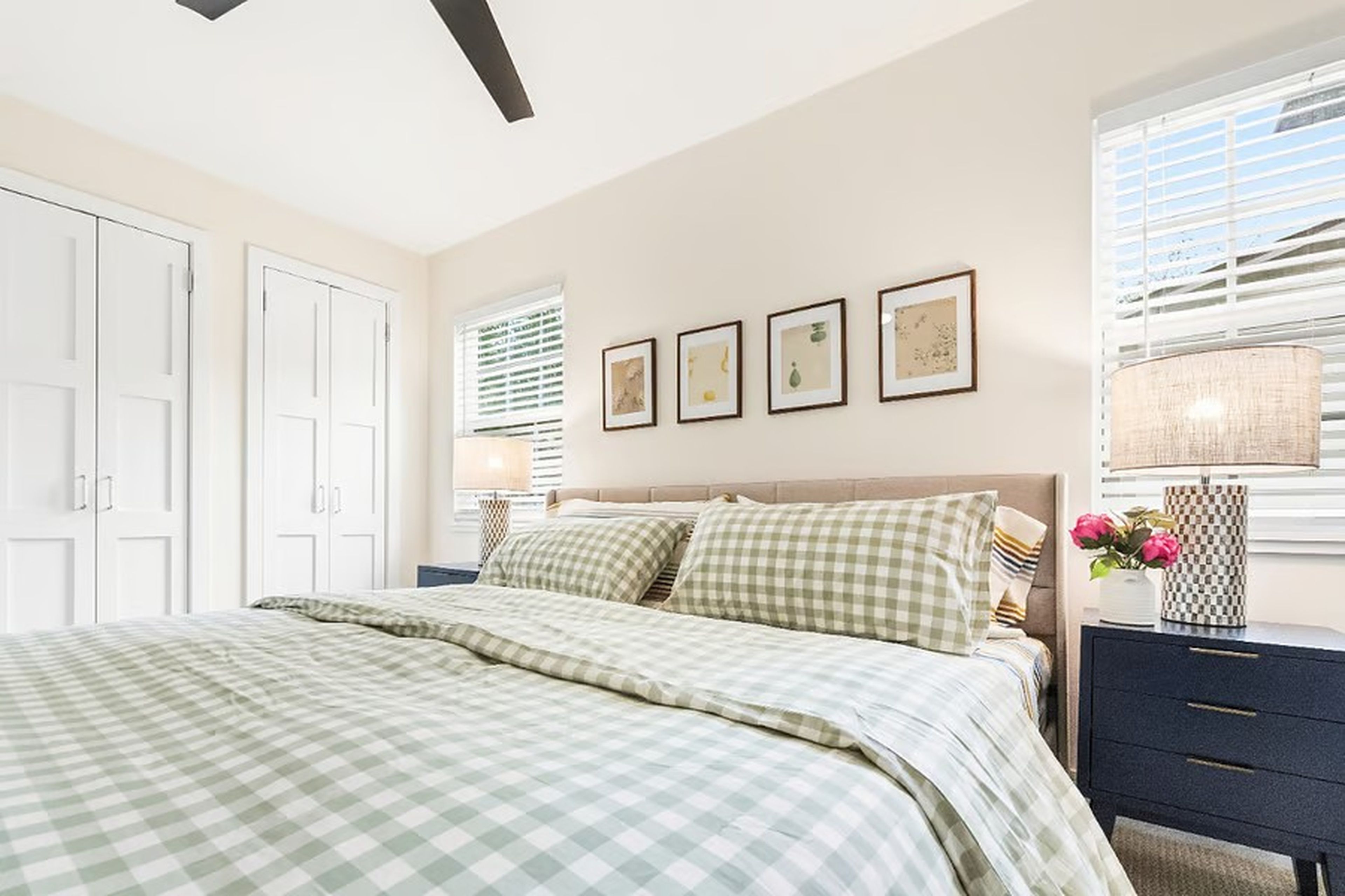 Un dormitorio con cama, mesita de noche, lámpara, ventana con persianas y puerta.