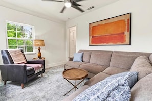 A living room with a sofa, armchair, coffee table, and a painting on the wall.