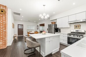 A modern kitchen with white cabinetry, a central island, bar stools, a stainless steel refrigerator, and a gas stove.