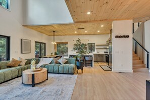 Un vaste espace de vie agrémenté d’un canapé vert, d’une table basse ronde en bois et d’une grande fenêtre.