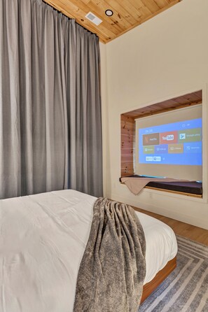 Une chambre avec un lit, une grande fenêtre et un écran fixé au mur qui diffuse des services de diffusion en continu.