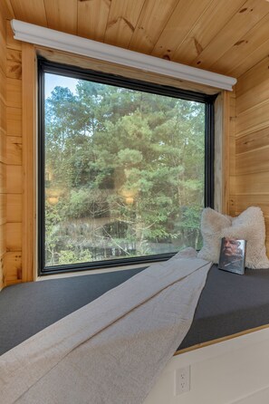 Une pièce avec une grande fenêtre, un banc recouvert d’une couverture et un livre posé sur un coussin.
