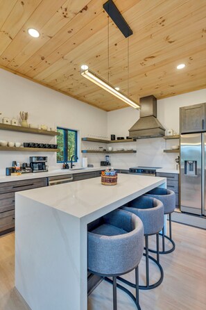A modern kitchen with a central island, bar stools, and a stainless steel refrigerator. - New Luxury Cabin - HotTub & Views - 5 min to Boone (Blowing Rock)